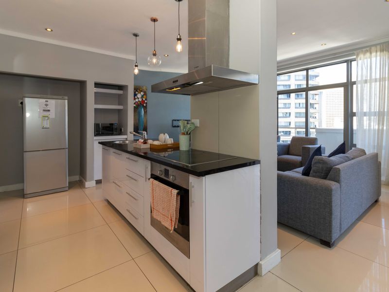 Modern open-plan kitchen featuring sleek white cabinetry, granite countertops, integrated appliances, and recessed lighting, seamlessly flowing into the adjacent living area.