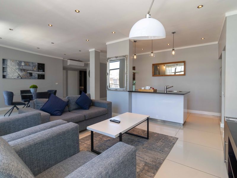 An open-plan living and kitchen area featuring tiled flooring, recessed lighting, and a central kitchen island with a sink.