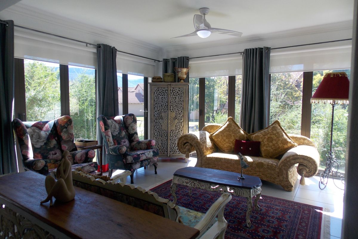 Bright and airy living room featuring large floor-to-ceiling windows, tiled flooring, and a modern ceiling fan, offering pleasant views of the surrounding garden.