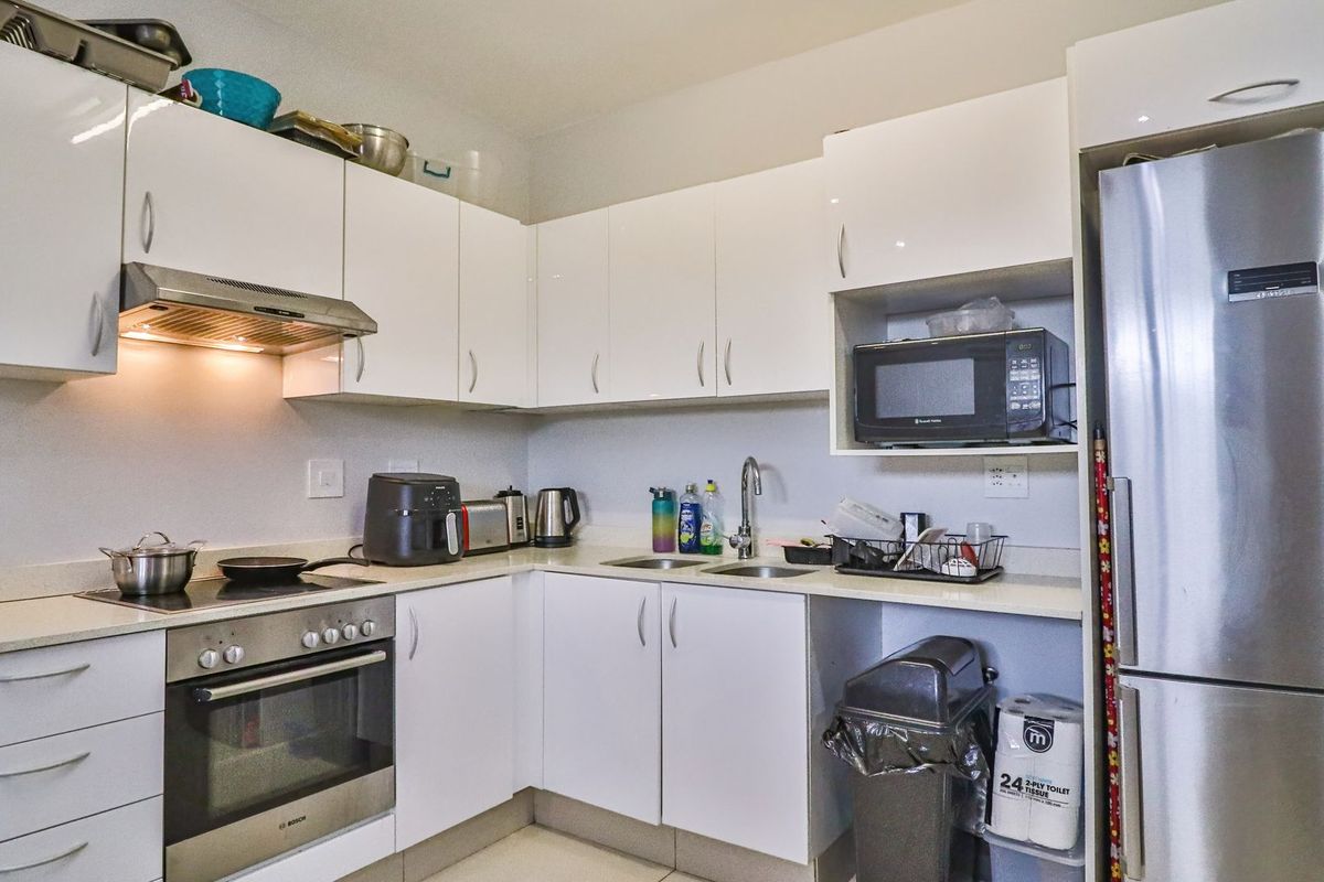 Modern kitchen featuring white high-gloss cabinetry, stone countertops, integrated stainless steel oven, electric hob, and extractor fan.
