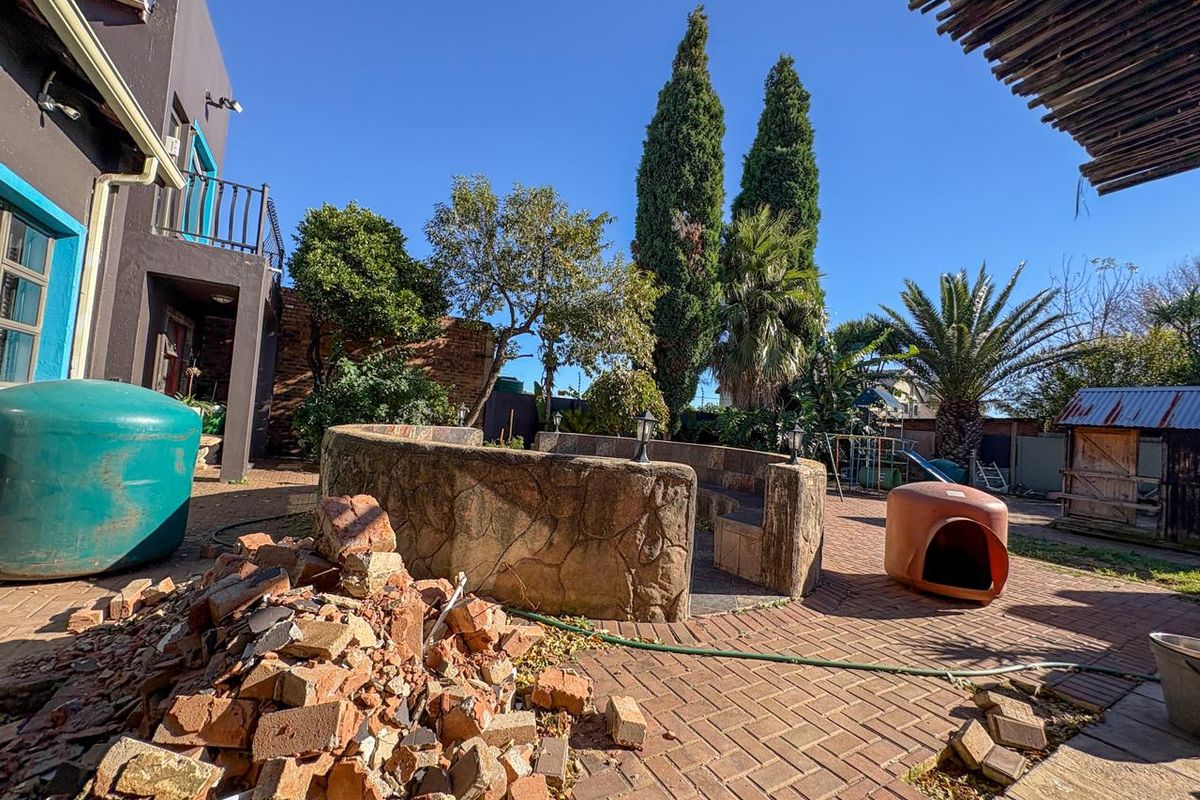 Rear garden area featuring a paved patio, built-in stone seating, and a water tank, requiring general site clearance and maintenance.