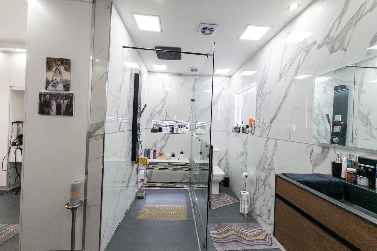 Modern bathroom featuring large-format marble-look wall tiles, a spacious walk-in shower with a rain shower head, and a contemporary vanity unit.