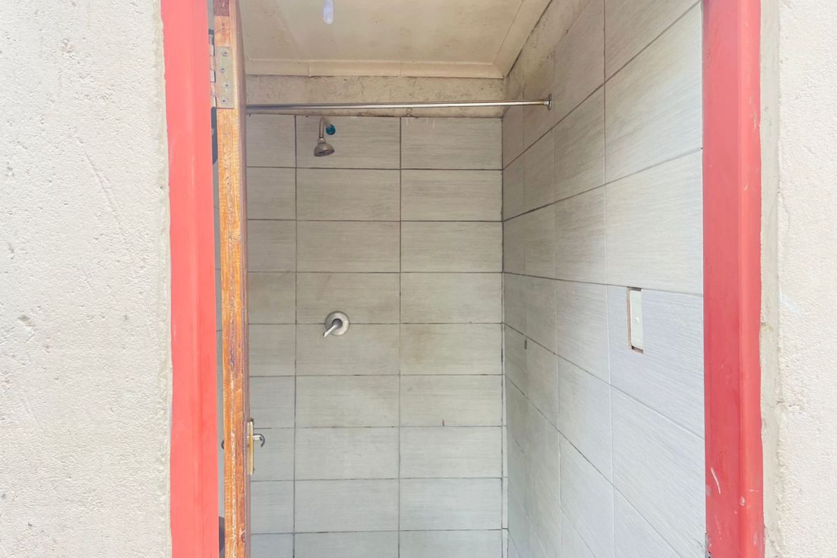 A compact shower area featuring tiled walls, a wall-mounted shower head, and a simple door entrance.