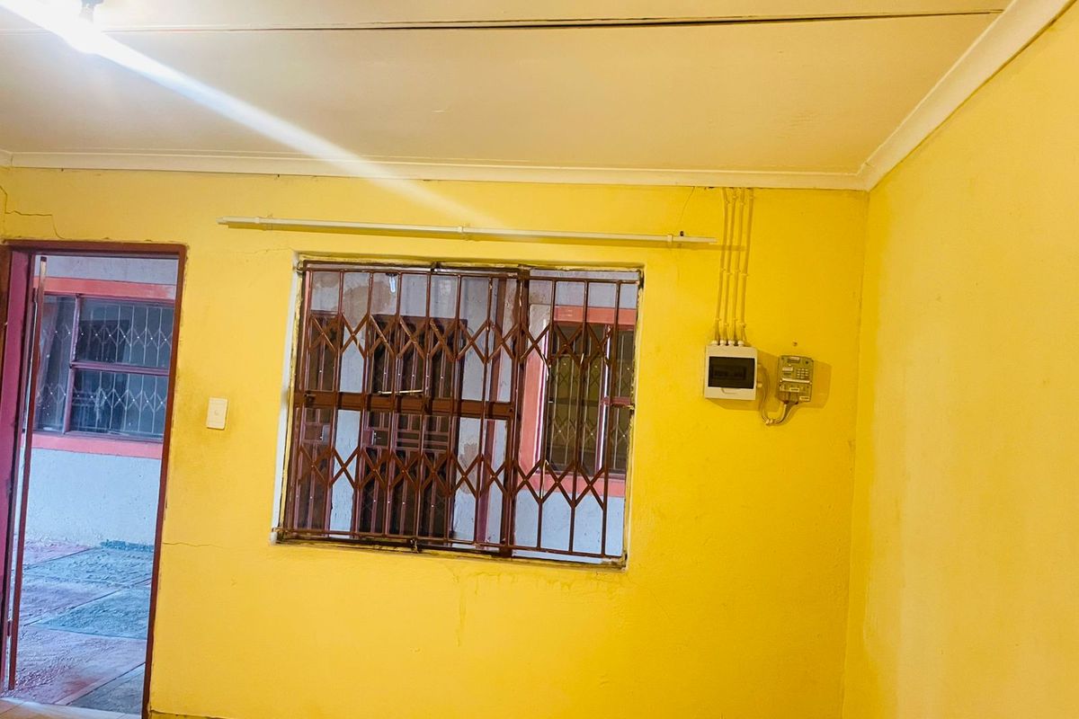 A basic interior room featuring yellow painted walls, a window with security bars, and exposed electrical wiring.