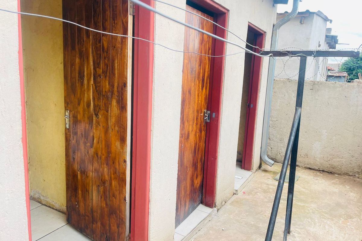 Exterior view of multiple utility or storage room entrances featuring wooden doors with red frames and a concrete courtyard area.
