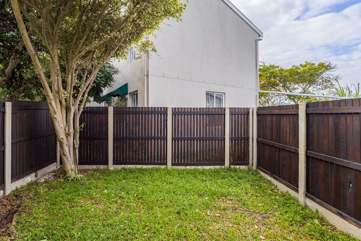 A private rear garden featuring a lawn area enclosed by dark timber fencing with concrete posts, adjacent to the townhouse exterior wall.