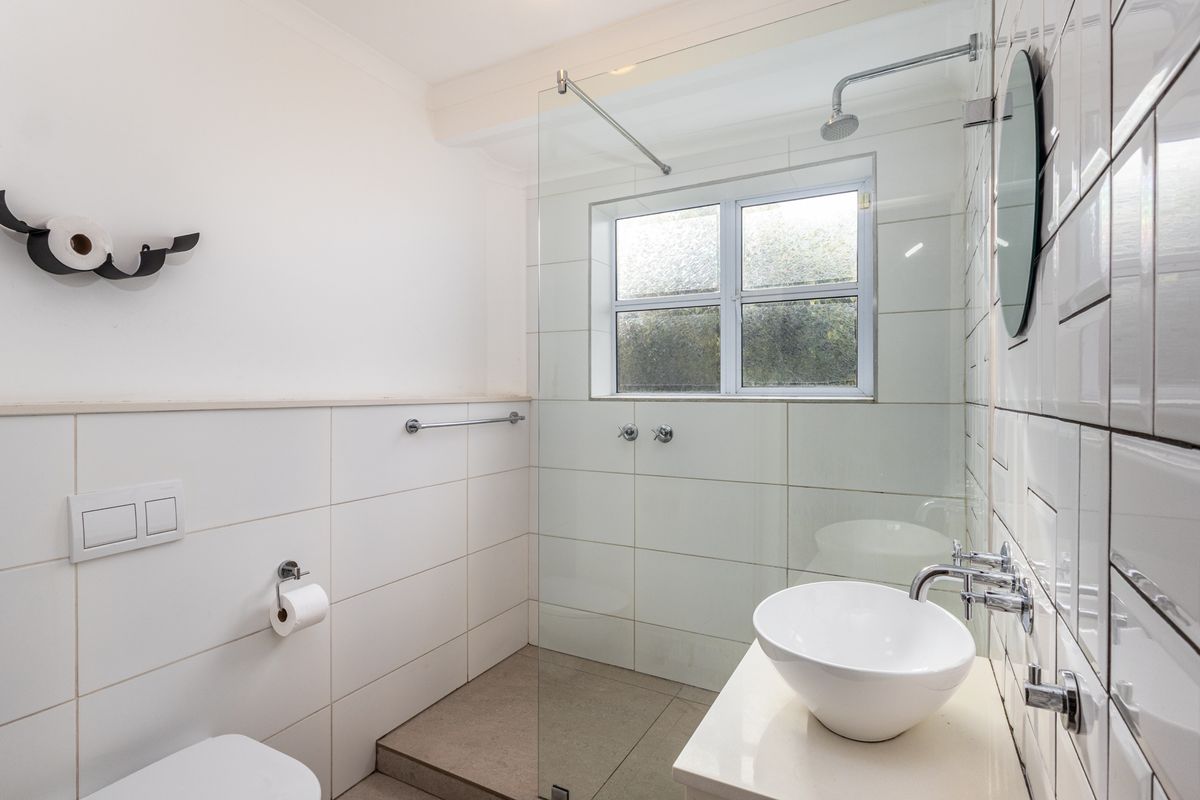 A modern bathroom featuring a glass-enclosed walk-in shower, a contemporary vessel sink, and clean white wall tiling.