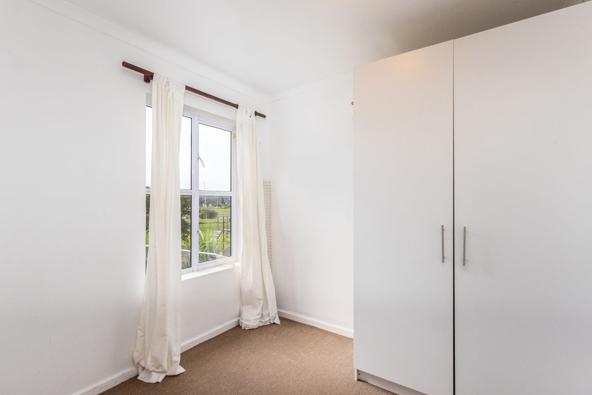 A bright bedroom featuring neutral carpeting and a built-in wardrobe, offering a clean and functional space with natural light.