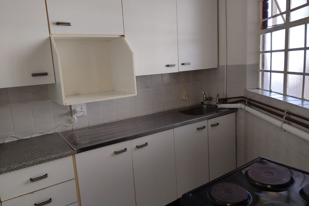 A functional kitchen featuring white cabinetry, a stainless steel sink, tiled splashbacks, and a built-in stove, with visible surface-mounted plumbing.