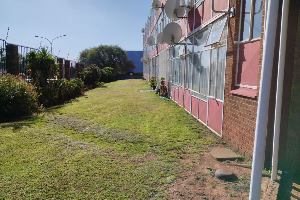 A view of the rear exterior of the flat complex, featuring a communal lawn area, brick facade, and multiple satellite dishes.