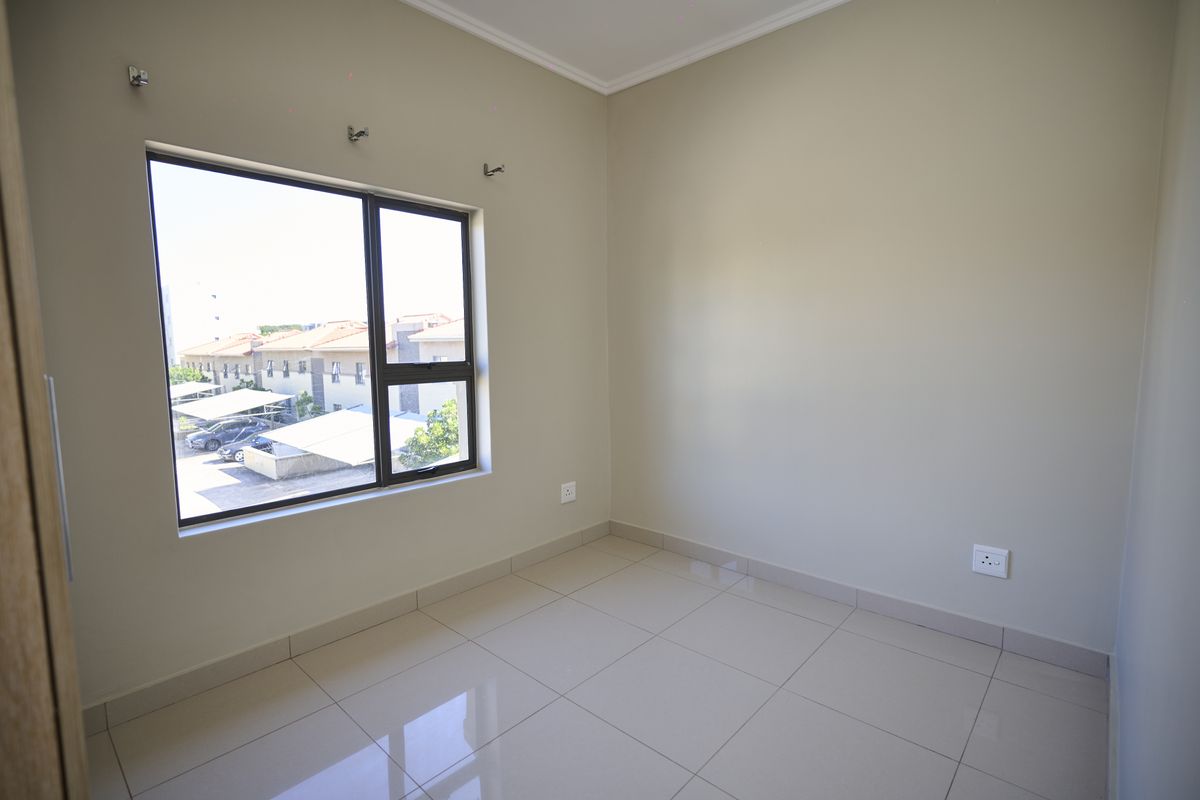 A bright, empty bedroom featuring neutral wall paint, large aluminium-framed windows, and clean tiled flooring, ready for personalization.