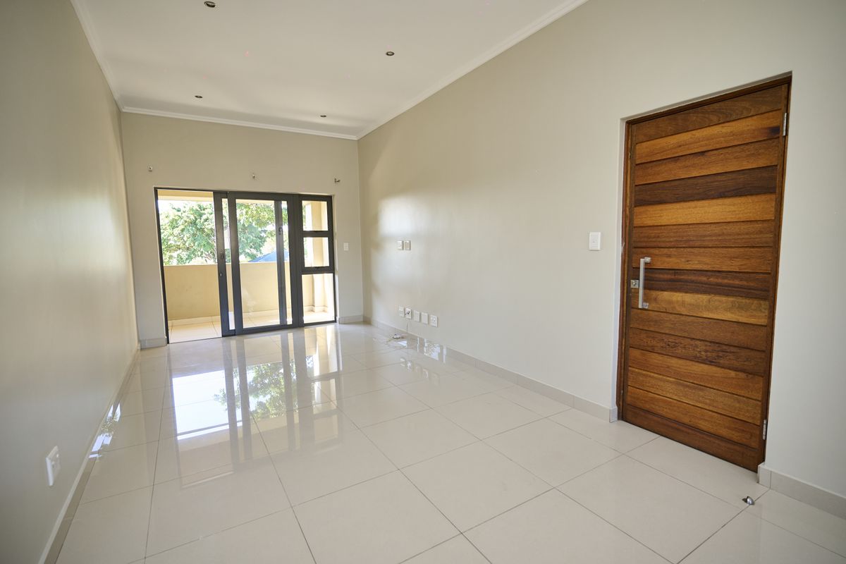 A bright, empty living room featuring polished tiled floors, recessed lighting, and a sliding glass door leading to an outdoor balcony.