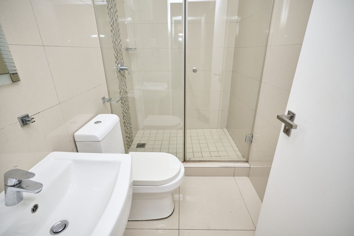 Modern bathroom featuring a glass-enclosed shower, wall-mounted basin, and toilet with neutral floor-to-ceiling tiling.