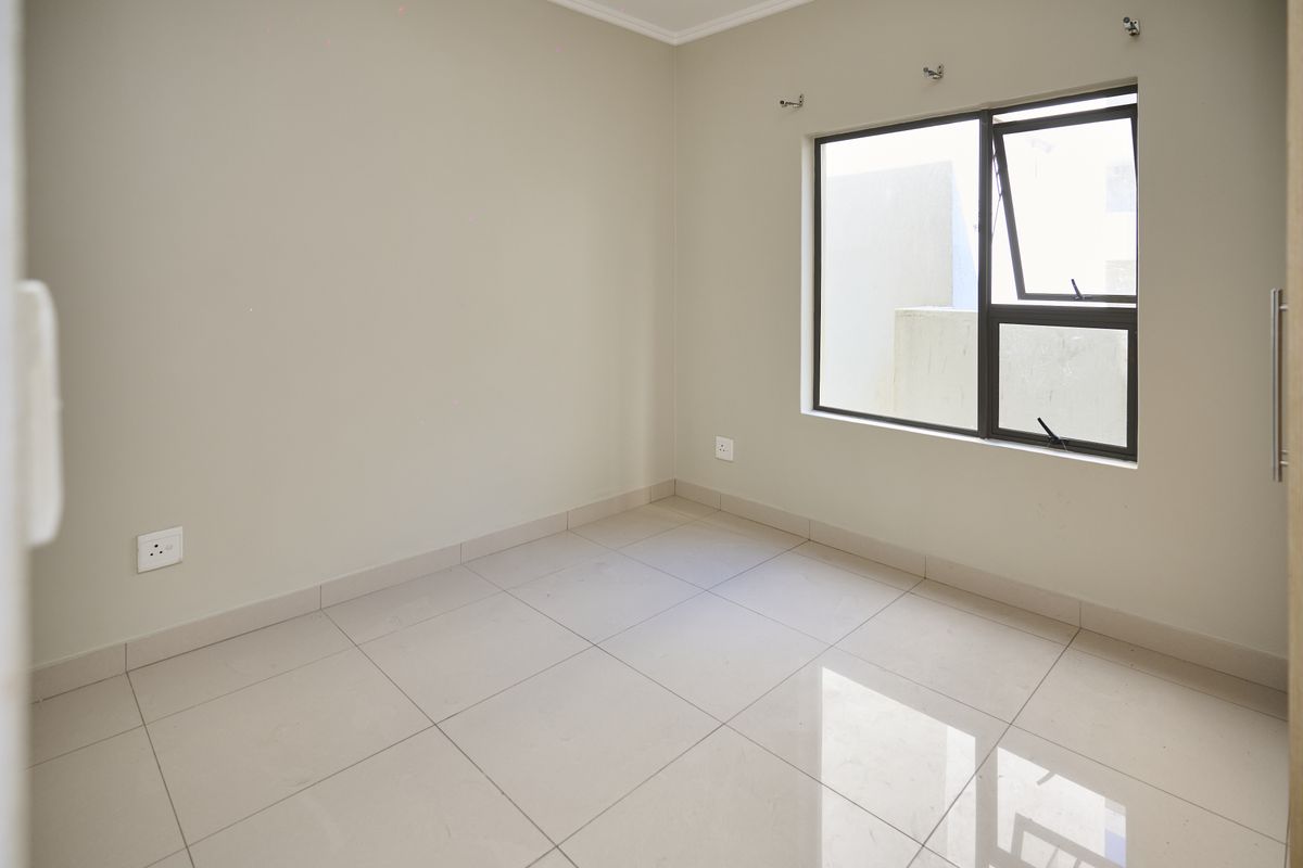 A bright, empty bedroom featuring neutral tiled flooring, light-colored walls, and a modern aluminum-framed window.