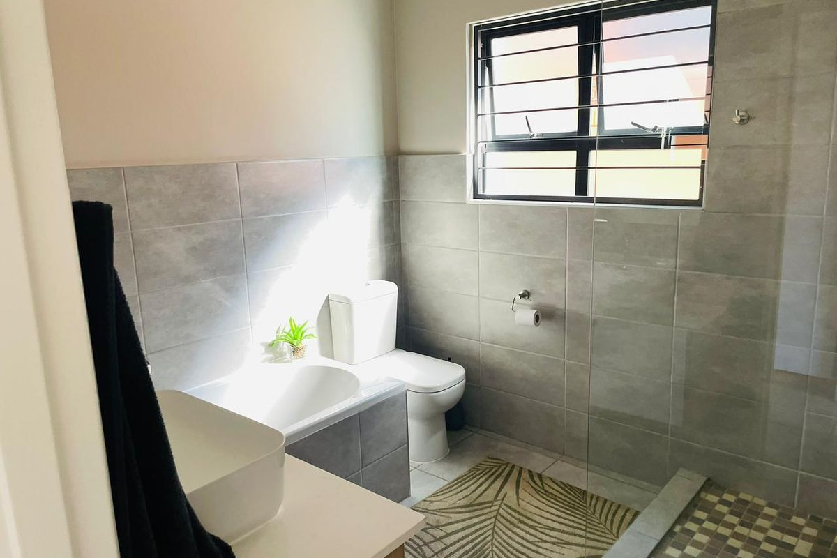 Modern bathroom featuring a glass-enclosed walk-in shower, tiled walls, a vanity basin, and a toilet with a window for natural light.