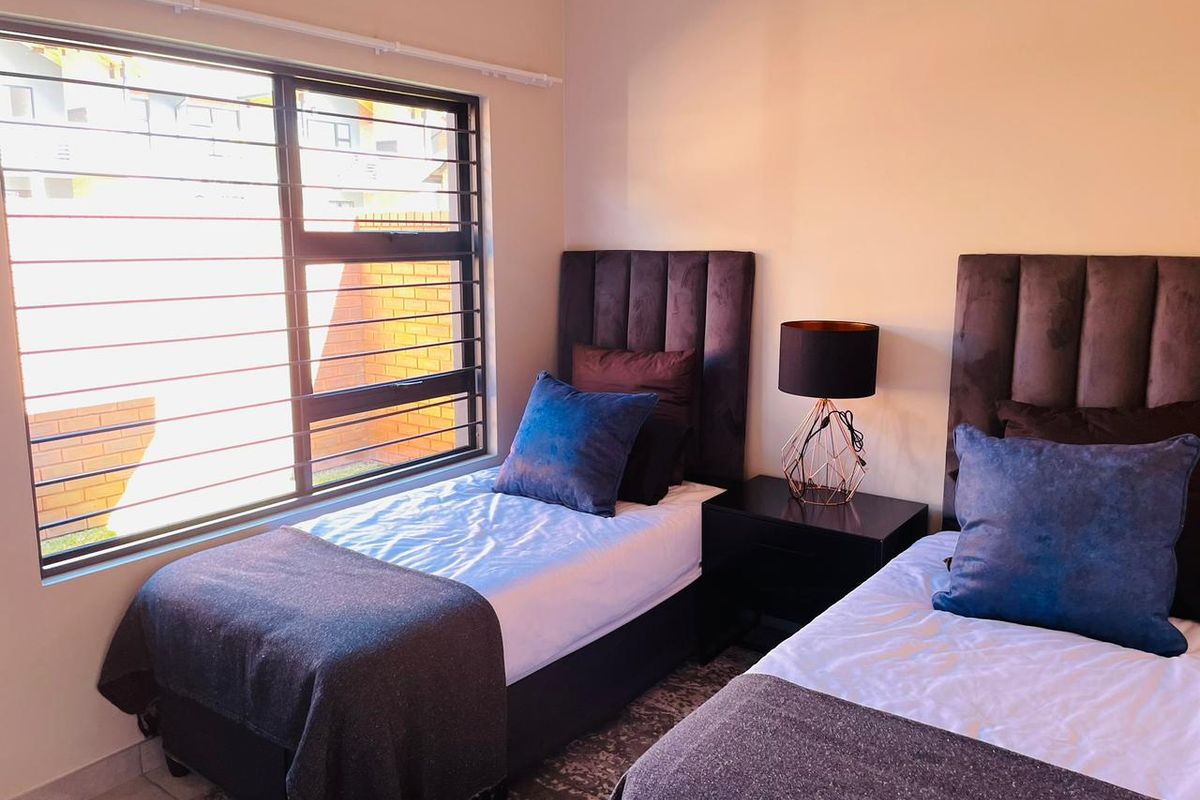 A well-lit bedroom featuring large windows with integrated security bars, neutral wall finishes, and tiled flooring.