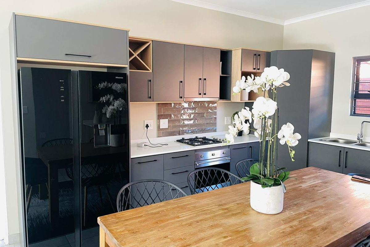 Modern kitchen featuring grey cabinetry, light wood accents, subway tile backsplash, built-in oven, gas hob, and integrated sink.