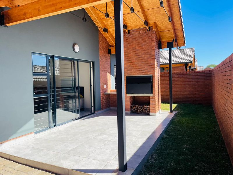 Covered patio area featuring a built-in brick braai, tiled flooring, and sliding glass doors leading into the interior living space.