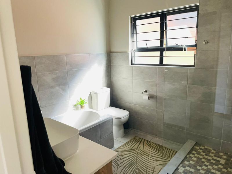 Modern bathroom featuring a glass-enclosed walk-in shower, tiled walls, a vanity basin, and a toilet with a window for natural light.