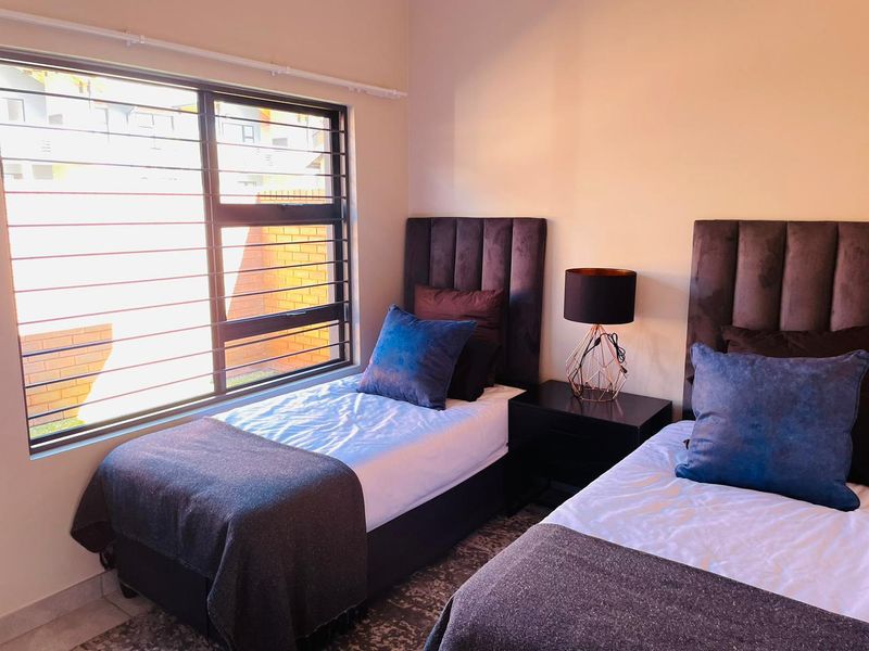 A well-lit bedroom featuring large windows with integrated security bars, neutral wall finishes, and tiled flooring.