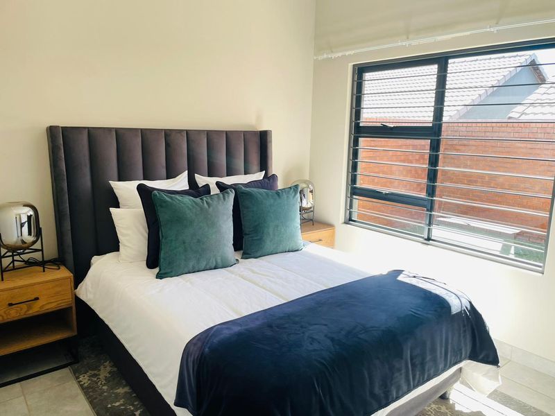 A well-lit bedroom featuring a large window with horizontal security bars and neutral wall finishes.