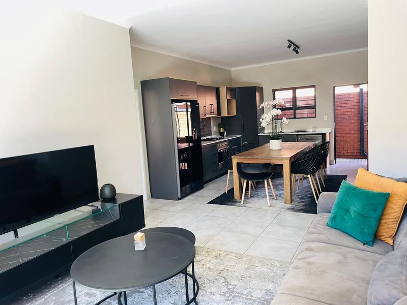 Open-plan living and dining area featuring a modern kitchen with dark cabinetry, tiled flooring, and direct access to an outdoor patio.