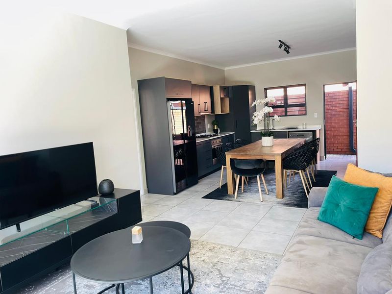 Open-plan living and dining area featuring a modern kitchen with dark cabinetry, tiled flooring, and direct access to an outdoor space.