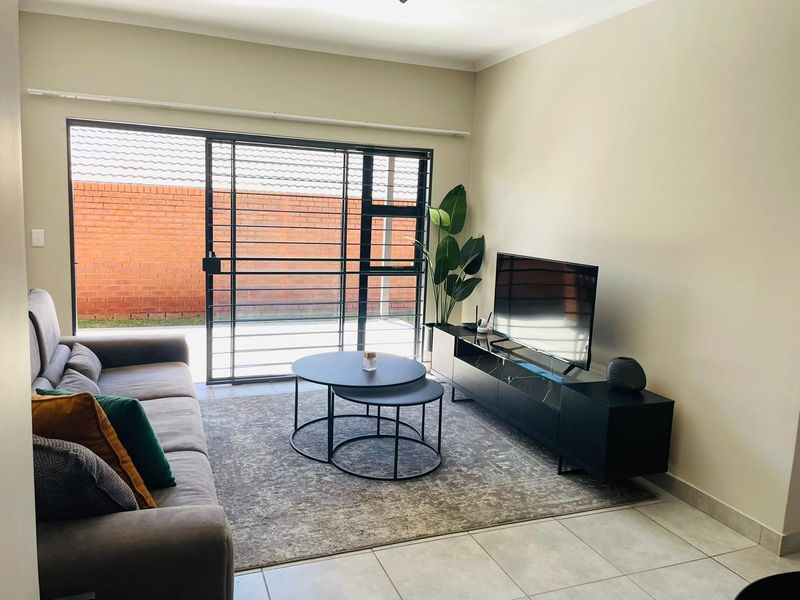 A bright living room featuring large sliding glass doors with security bars, leading to an outdoor area with a brick boundary wall.