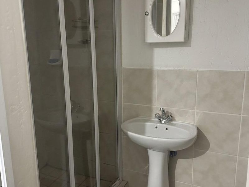 A functional bathroom featuring a pedestal basin, a glass-enclosed shower, and a wall-mounted medicine cabinet with neutral ceramic tiling.