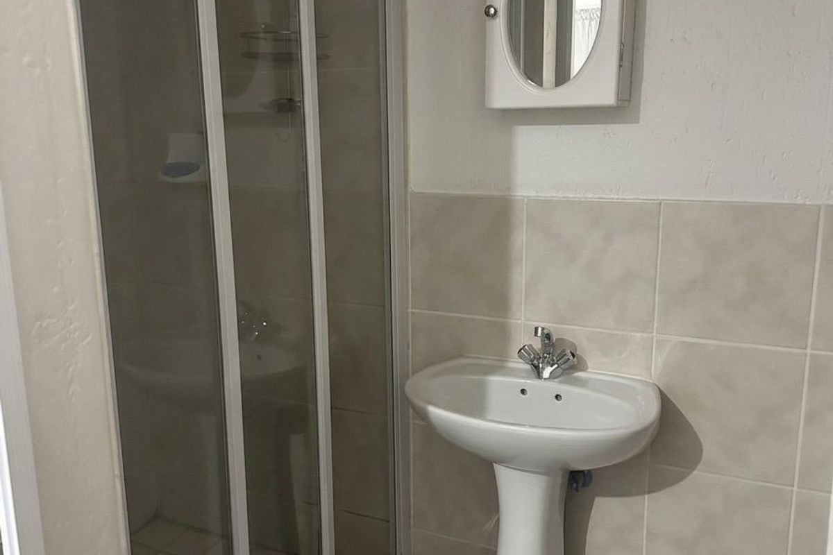 A functional bathroom featuring a pedestal basin, a glass-enclosed shower, and a wall-mounted medicine cabinet with neutral ceramic tiling.
