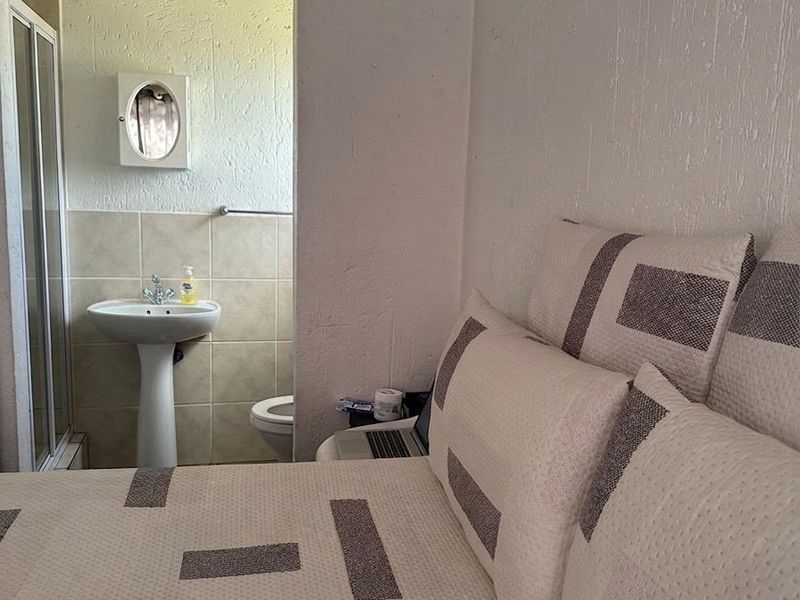 A bedroom featuring an en-suite bathroom with a pedestal basin, shower enclosure, and toilet, finished with textured walls.