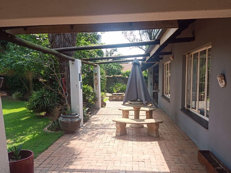 A covered outdoor patio area featuring brick paving and a timber pergola, overlooking a landscaped garden space.