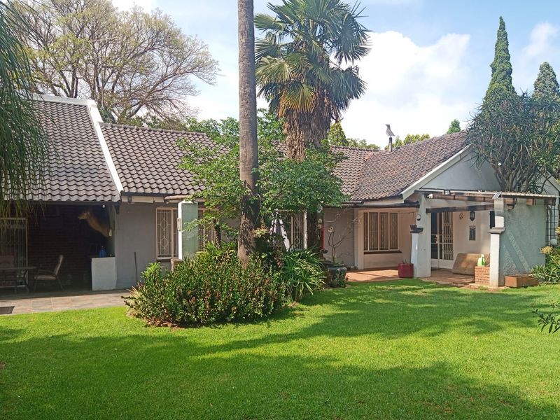 Rear view of the house featuring a tiled roof, covered patio areas, and a well-maintained garden with mature trees.