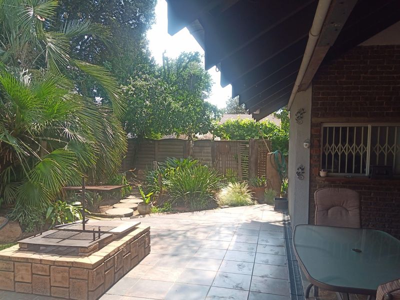 A covered patio area featuring a built-in brick braai, tiled flooring, and direct access to a landscaped garden.