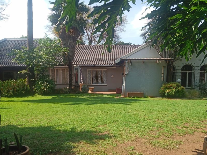 A view of the rear garden and house exterior, featuring a well-maintained lawn, mature trees, and a tiled roof structure.