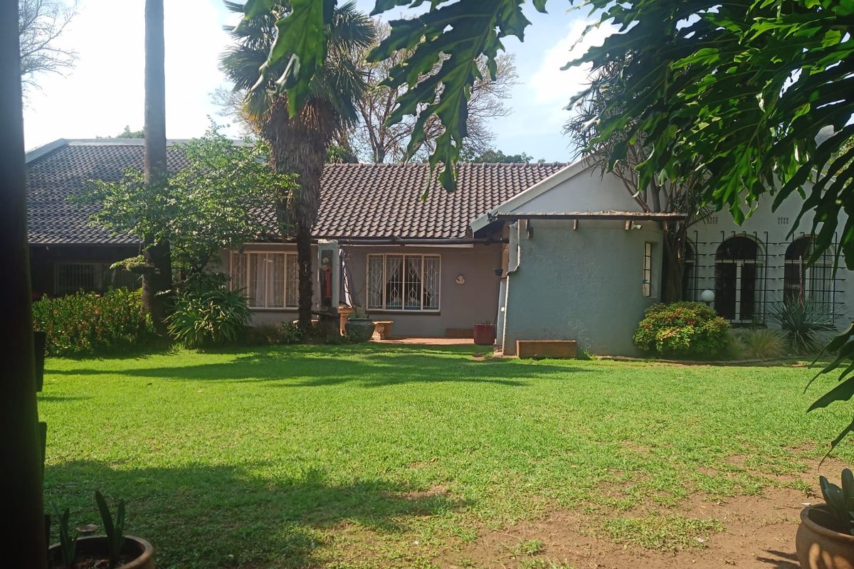 A view of the rear garden and house exterior, featuring a well-maintained lawn, mature trees, and a tiled roof structure.