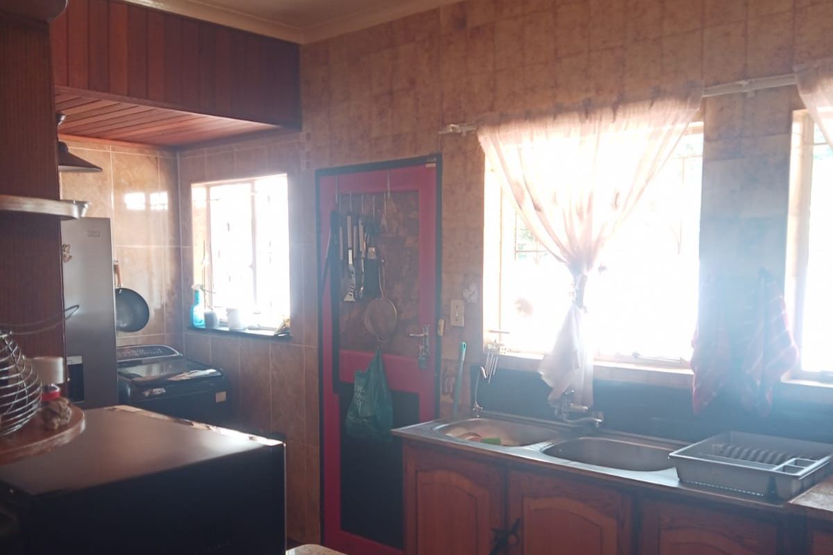 A functional kitchen featuring fitted wooden cabinetry, a double bowl sink, and tiled splashbacks, offering potential for a modern renovation.