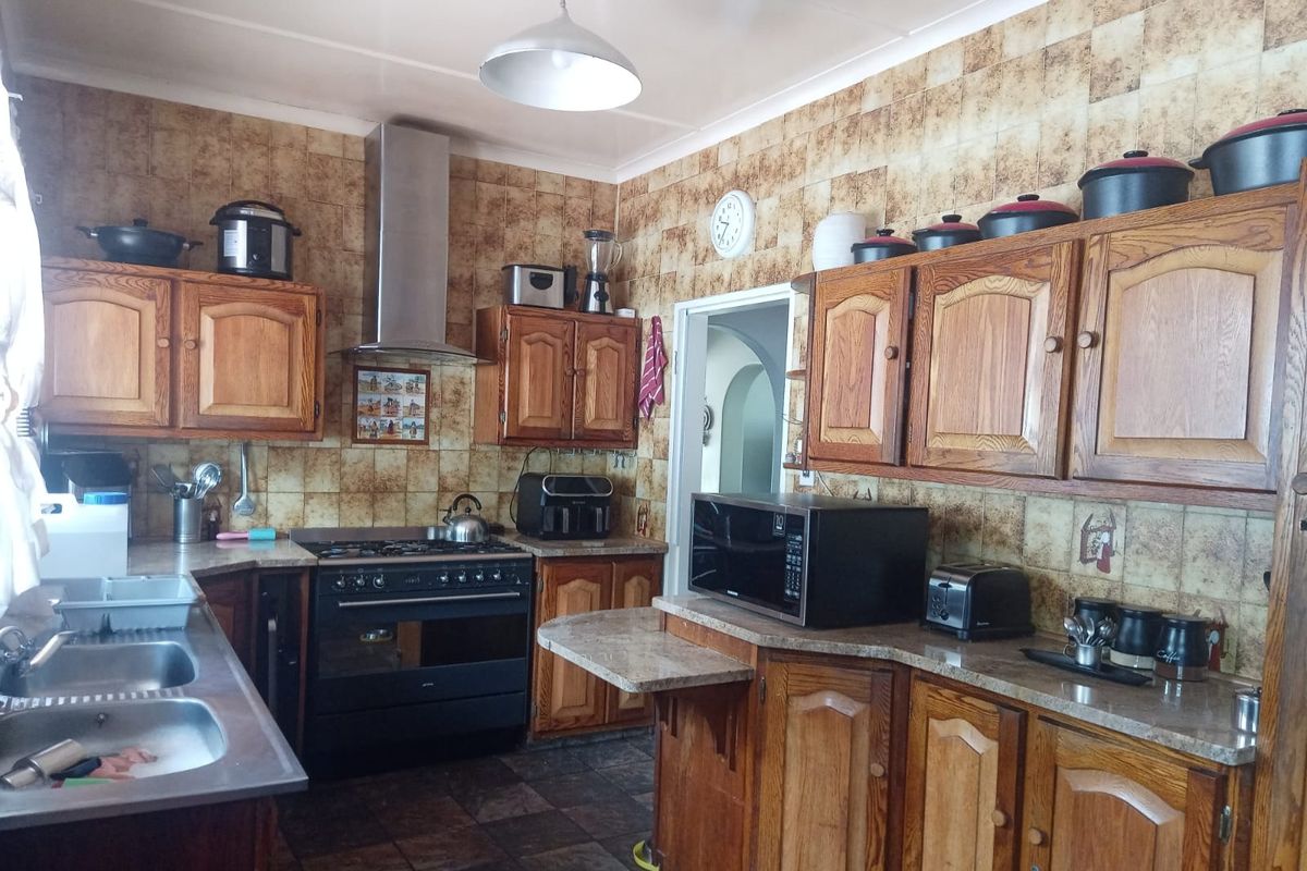 A functional kitchen featuring traditional wooden cabinetry, a gas stove with extractor fan, and a double bowl sink with tiled splashback.