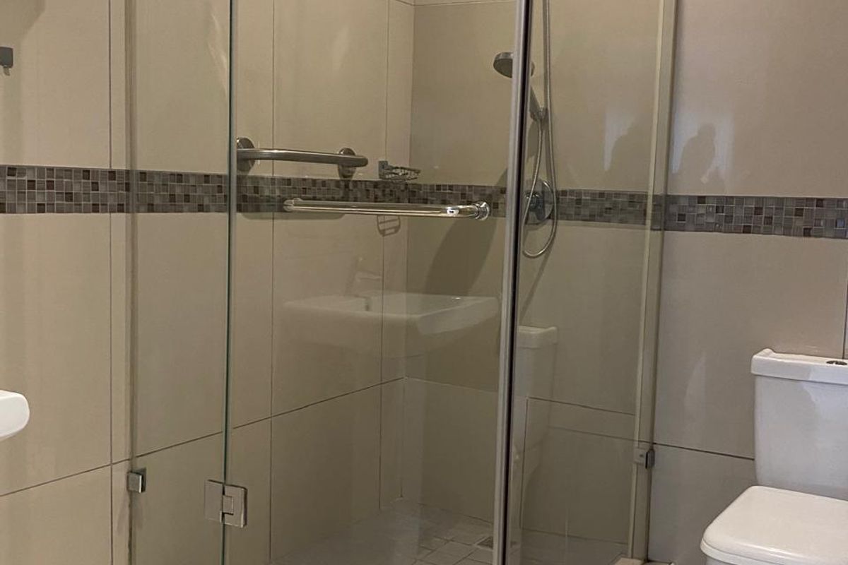 Modern bathroom featuring a glass-enclosed shower with chrome fixtures, tiled walls with a decorative mosaic border, and a standard white toilet.