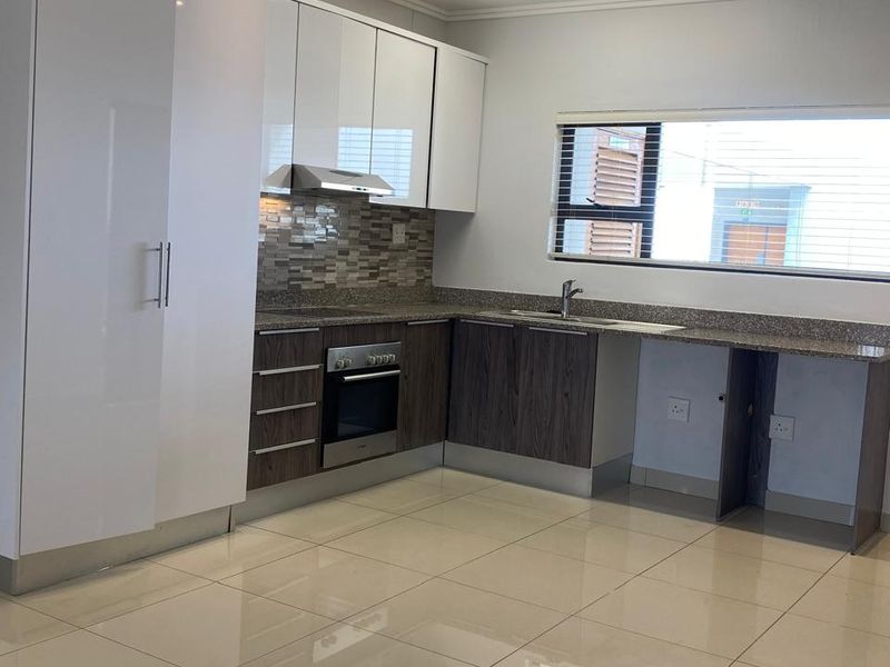 Modern kitchen featuring high-gloss white upper cabinetry, wood-grain lower cabinets, granite countertops, built-in oven, extractor fan, and polished porcelain floor tiles.