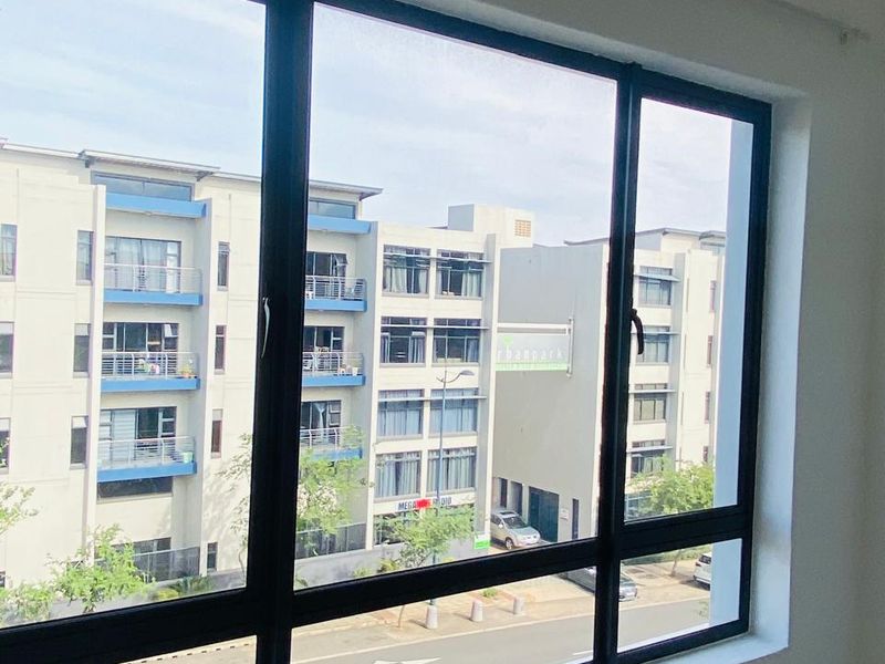 A bright bedroom featuring large black-framed windows that offer a clear view of the surrounding apartment complex and street.