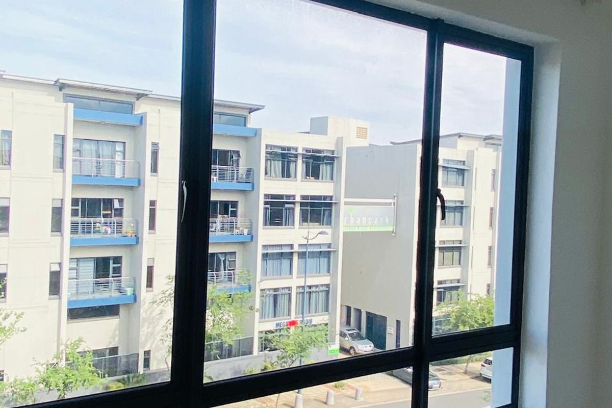 A bright bedroom featuring large black-framed windows that offer a clear view of the surrounding apartment complex and street.