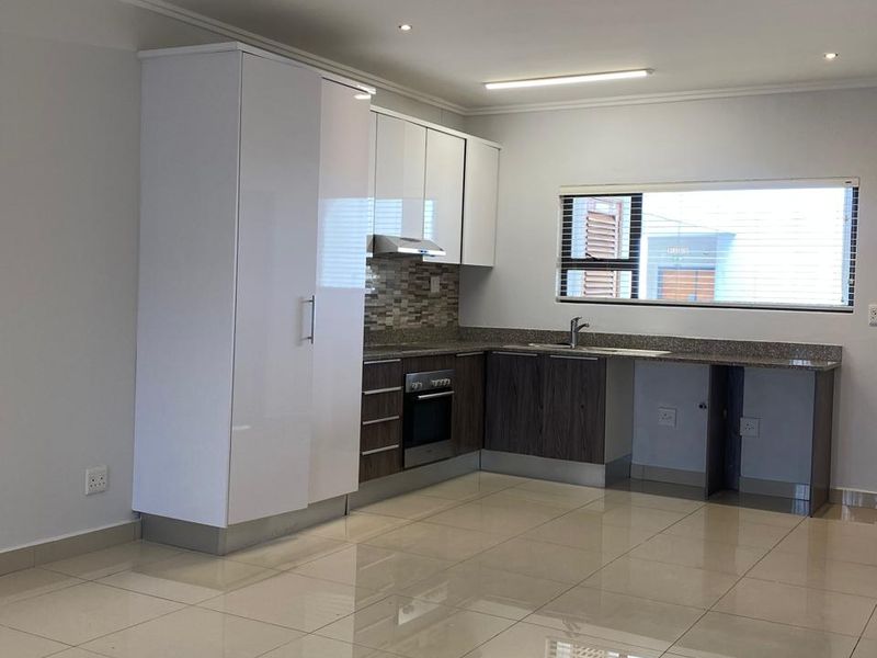 Modern open-plan kitchen featuring high-gloss white cabinetry, dark wood-finish base units, granite countertops, and integrated oven with extractor fan.