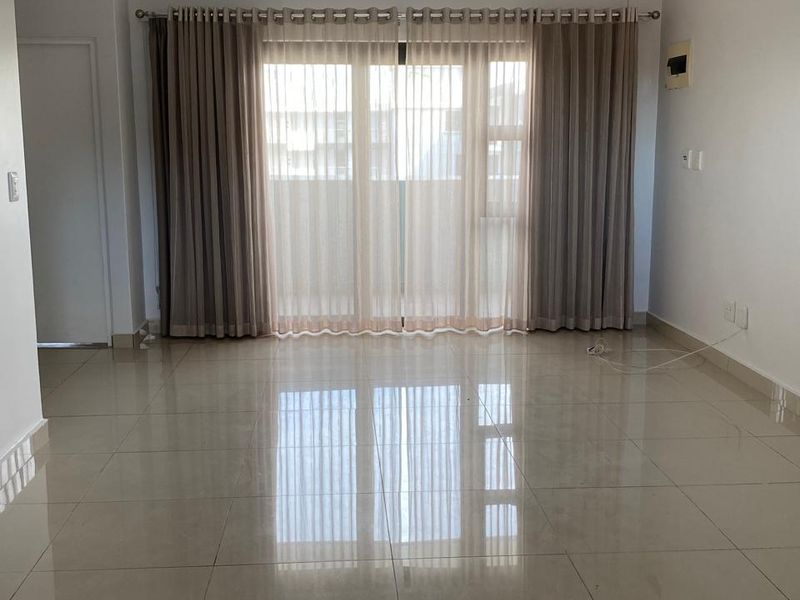 A bright and spacious open-plan living area featuring polished porcelain floor tiles, recessed downlighting, and large sliding glass doors leading to a balcony.