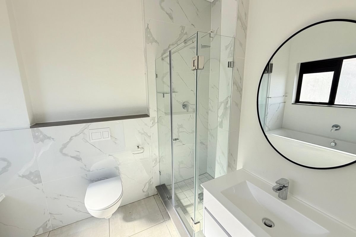 Modern bathroom featuring marble-look wall tiles, a glass-enclosed shower, wall-mounted toilet, and a sleek vanity with a circular mirror.