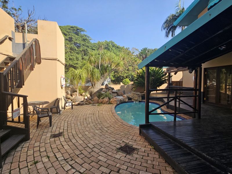 Outdoor pool area featuring a paved patio, wooden decking, and a covered pergola, providing a functional space for relaxation and outdoor entertainment.