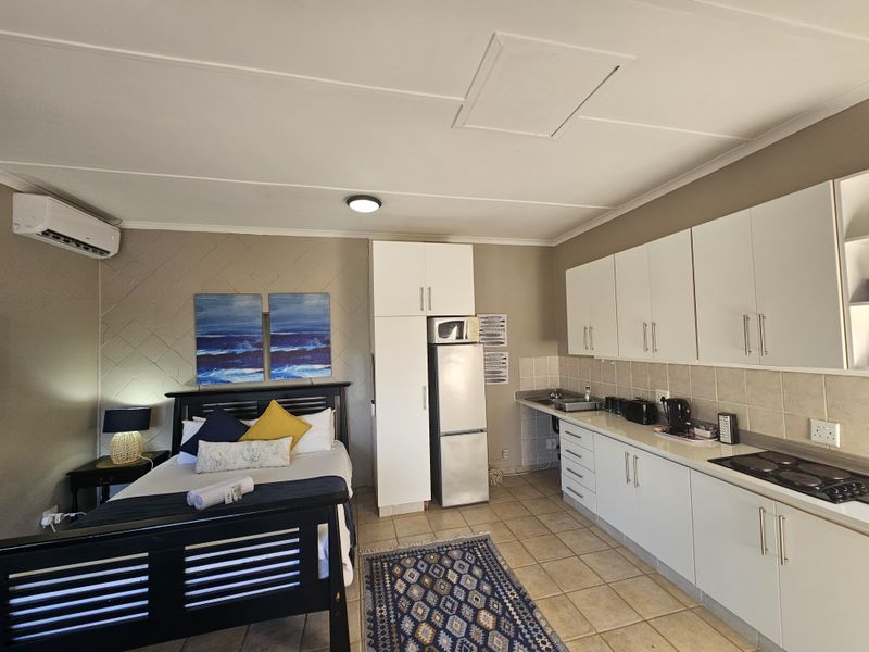 Open-plan studio apartment featuring a combined bedroom and kitchenette area with white cabinetry, tiled flooring, and a wall-mounted air conditioning unit.