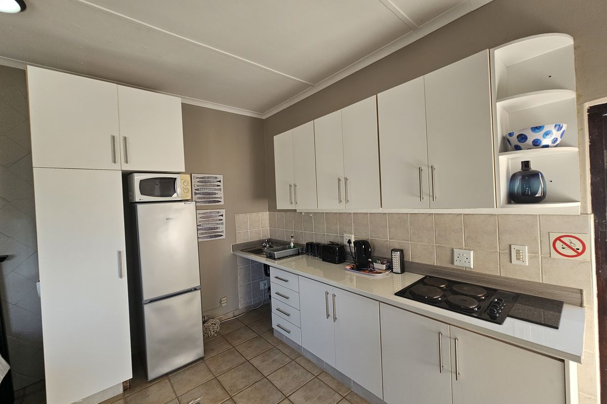 A functional kitchen featuring white cabinetry, laminate countertops, a tiled backsplash, and a built-in electric hob with tiled flooring throughout.