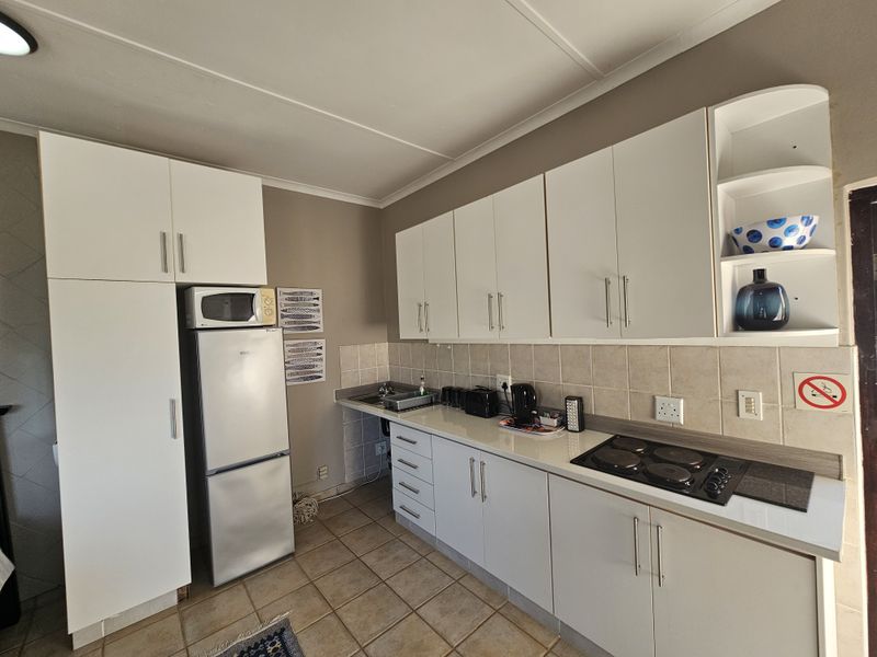 A functional kitchen featuring white cabinetry, laminate countertops, a tiled backsplash, and a built-in electric hob with tiled flooring throughout.
