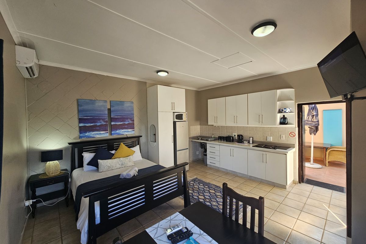 An open-plan studio apartment featuring a combined bedroom and kitchenette area with tiled floors, built-in cabinetry, and direct access to an outdoor patio.